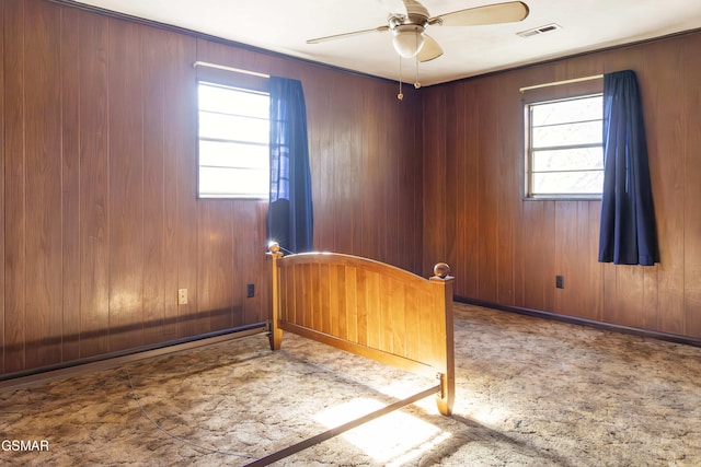 spare room with ceiling fan, plenty of natural light, and wooden walls