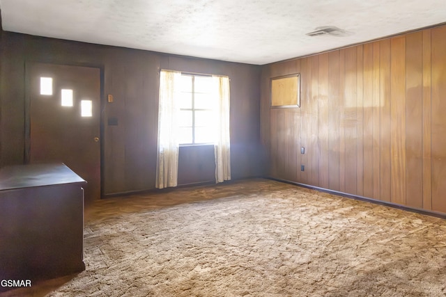 entryway with wood walls, a textured ceiling, and dark colored carpet