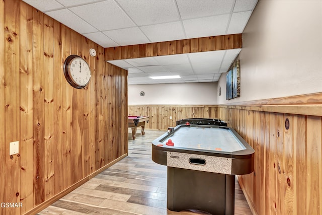 recreation room with wooden walls, wood finished floors, a drop ceiling, and wainscoting