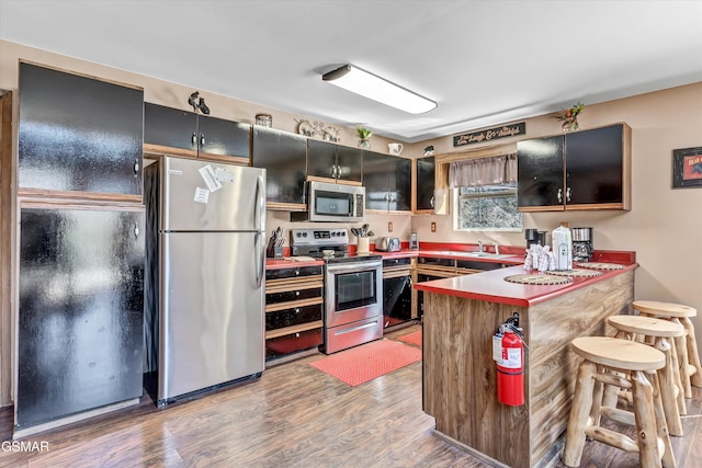 kitchen with a kitchen breakfast bar, dark cabinetry, a peninsula, appliances with stainless steel finishes, and wood finished floors