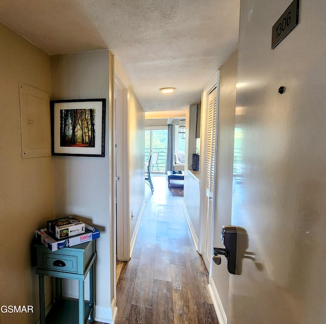 hall with hardwood / wood-style floors, a textured ceiling, and electric panel