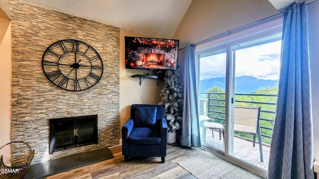 living area featuring hardwood / wood-style floors, a stone fireplace, and vaulted ceiling