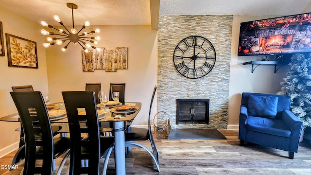 dining space with hardwood / wood-style flooring, a stone fireplace, a textured ceiling, and a chandelier