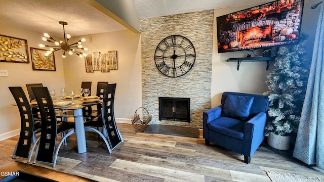 dining space featuring a chandelier, hardwood / wood-style floors, a textured ceiling, and a stone fireplace