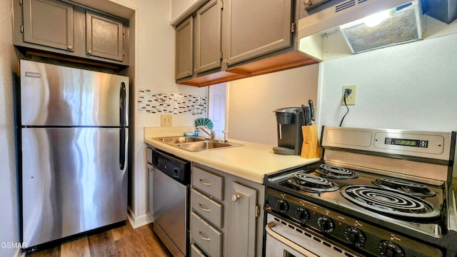 kitchen featuring gray cabinetry, sink, decorative backsplash, exhaust hood, and appliances with stainless steel finishes