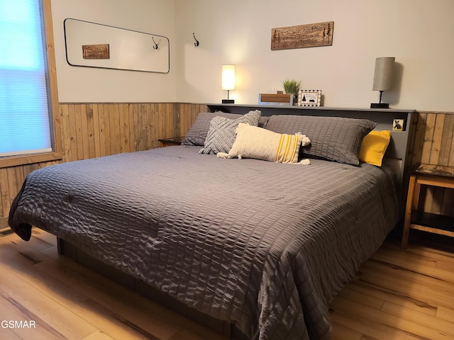 bedroom featuring wooden walls, wainscoting, and hardwood / wood-style floors