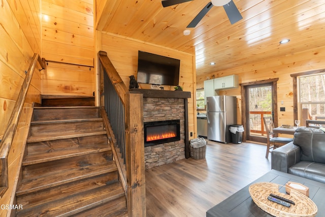 staircase with a stone fireplace, wooden walls, ceiling fan, hardwood / wood-style flooring, and wooden ceiling