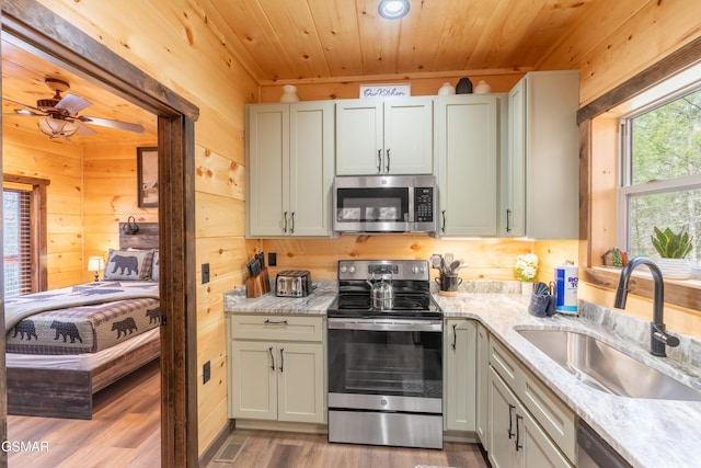 kitchen featuring wood ceiling, stainless steel appliances, wooden walls, sink, and light stone counters