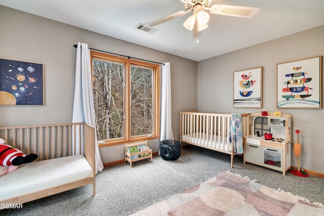 carpeted bedroom featuring a nursery area, visible vents, baseboards, and a ceiling fan