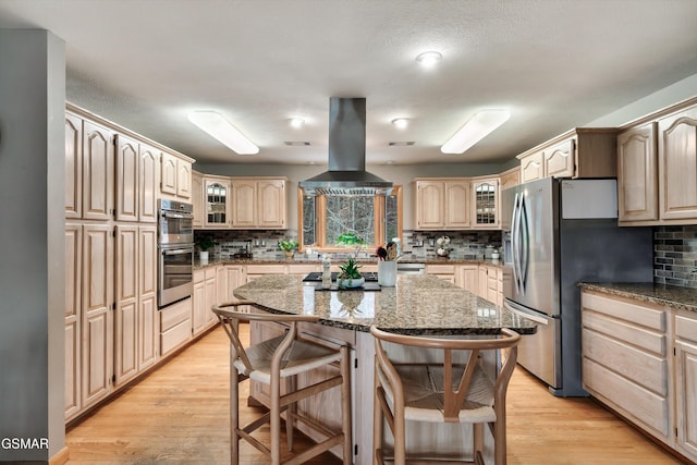 kitchen with stone counters, island range hood, stainless steel appliances, a kitchen island, and glass insert cabinets