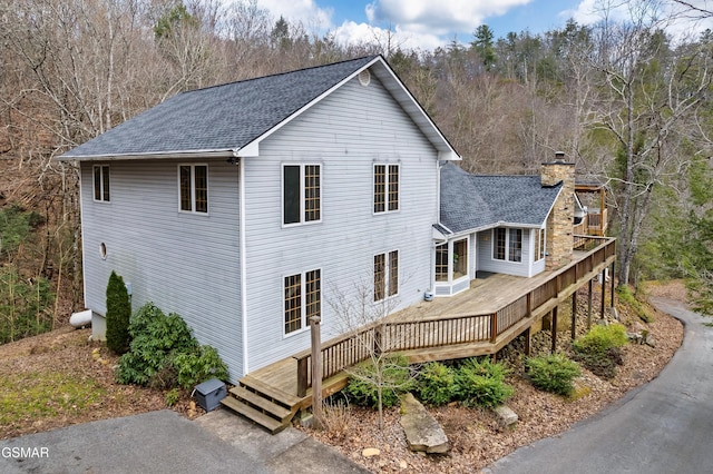 view of home's exterior featuring roof with shingles, a chimney, and a wooden deck