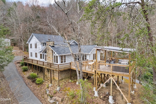 back of house with a wooded view, a shingled roof, and a wooden deck