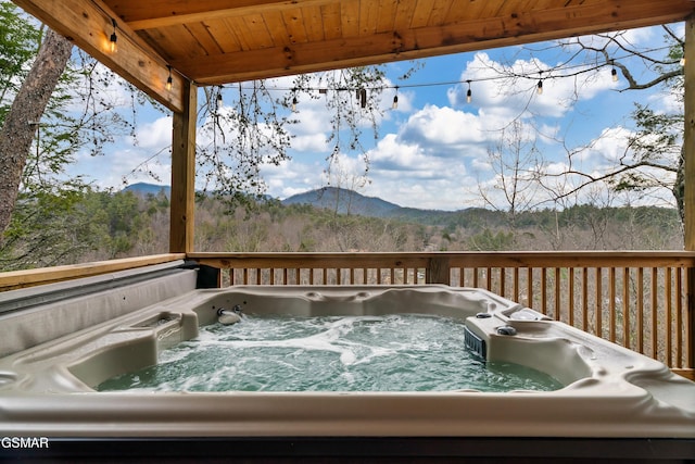 wooden deck with a mountain view, a hot tub, and a forest view