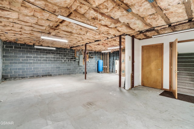 unfinished basement featuring concrete block wall and stairway