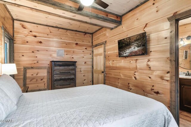 bedroom featuring beam ceiling, wooden walls, a sink, and wood finished floors