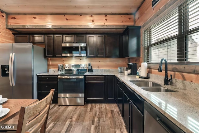 kitchen with a sink, light stone counters, light wood-style floors, and stainless steel appliances