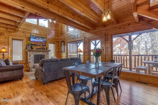 dining room with beamed ceiling, light hardwood / wood-style flooring, a stone fireplace, and wood ceiling