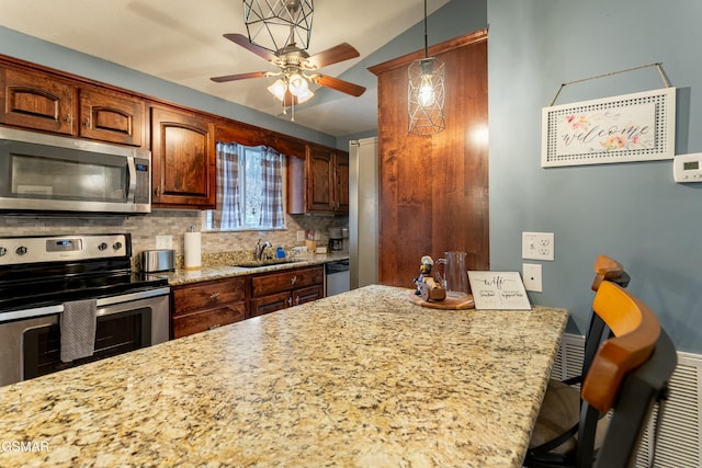 kitchen featuring pendant lighting, sink, stainless steel appliances, light stone counters, and tasteful backsplash