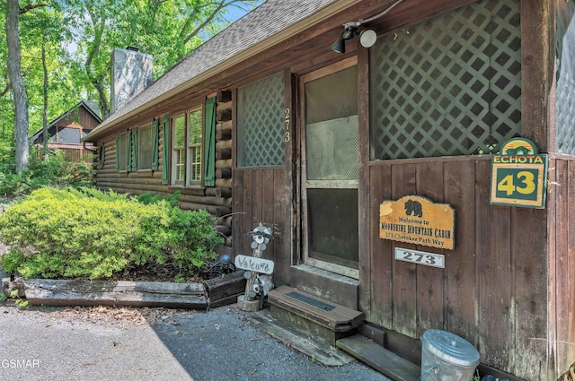 entrance to property featuring roof with shingles, log siding, and a chimney