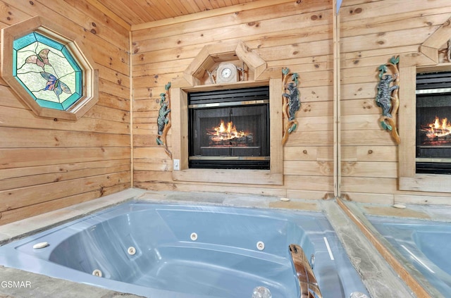 full bathroom featuring wooden walls, a warm lit fireplace, a tub with jets, and wood ceiling