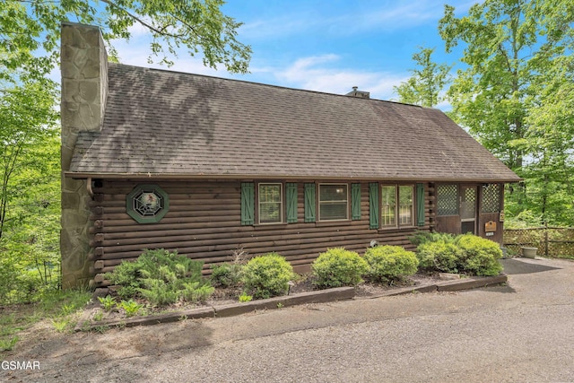 cabin featuring roof with shingles, a chimney, and log siding