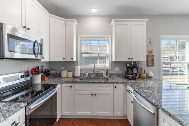 kitchen featuring white cabinets, appliances with stainless steel finishes, dark hardwood / wood-style flooring, dark stone countertops, and sink