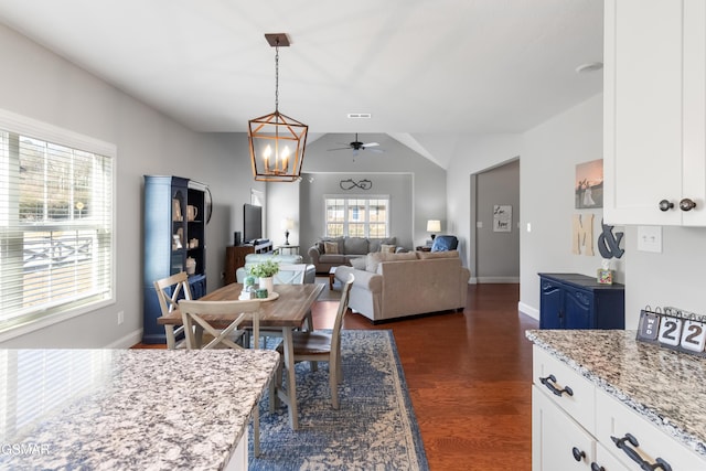 dining area featuring ceiling fan with notable chandelier, dark hardwood / wood-style floors, and vaulted ceiling