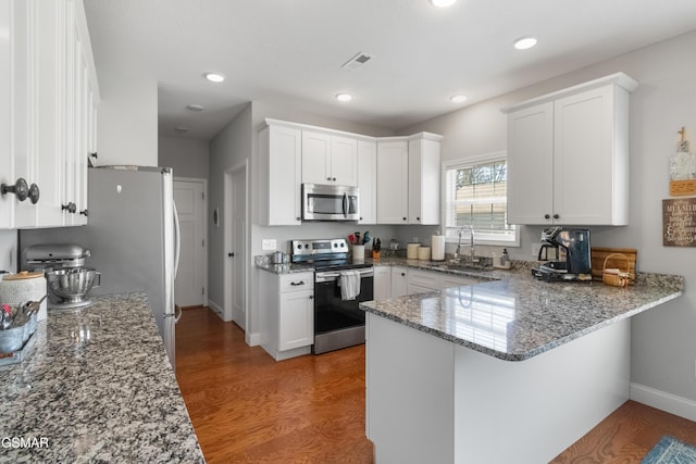 kitchen with wood-type flooring, white cabinets, sink, kitchen peninsula, and stainless steel appliances