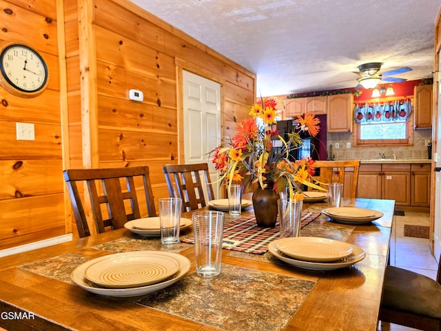 dining area featuring wood walls, a textured ceiling, and ceiling fan