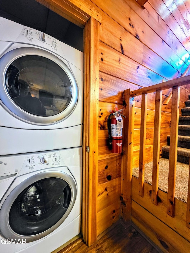 laundry area featuring dark wood-style flooring, laundry area, wood walls, and stacked washer / drying machine
