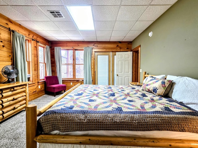 bedroom with wooden walls, visible vents, a paneled ceiling, and carpet