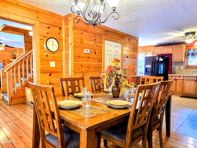 dining room featuring a textured ceiling, ceiling fan with notable chandelier, wooden walls, and light wood-style floors