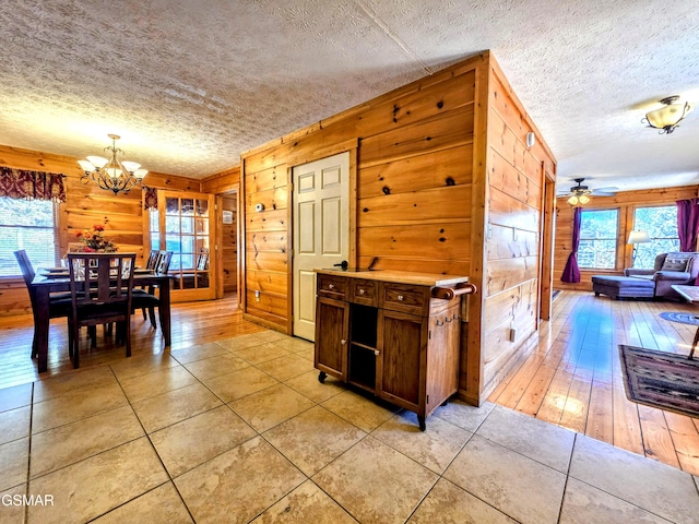 kitchen with ceiling fan with notable chandelier, light tile patterned floors, a textured ceiling, wood walls, and light countertops