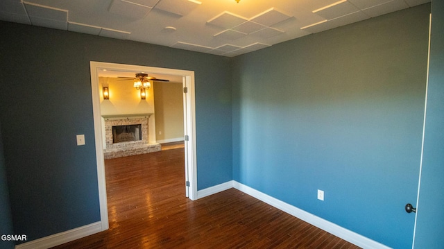 spare room featuring ceiling fan, dark hardwood / wood-style flooring, and a brick fireplace