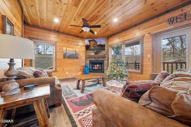 living room featuring wood ceiling, wooden walls, a stone fireplace, and plenty of natural light