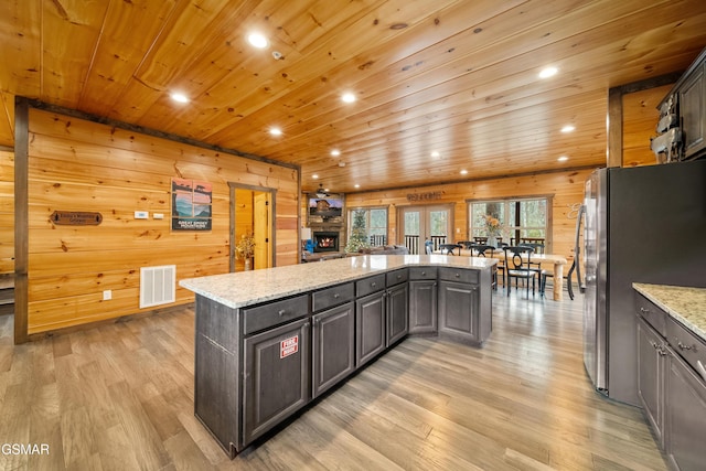 kitchen featuring light stone counters, a center island, dark brown cabinets, light hardwood / wood-style flooring, and stainless steel fridge