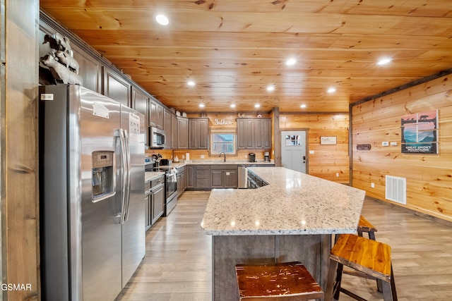 kitchen with sink, stainless steel appliances, light stone countertops, a kitchen island, and wooden ceiling