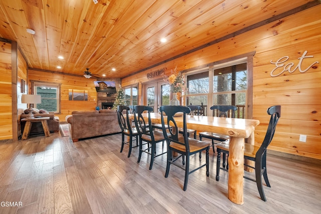 dining room with french doors, a stone fireplace, light hardwood / wood-style flooring, wooden ceiling, and wooden walls