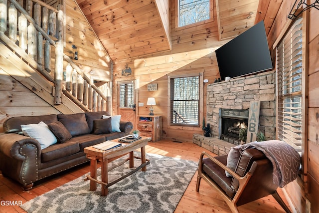 living room featuring hardwood / wood-style flooring, wood walls, wood ceiling, and a stone fireplace