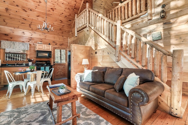 living room with wood ceiling, light wood-type flooring, a notable chandelier, wooden walls, and high vaulted ceiling