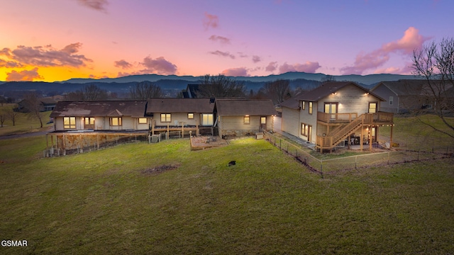 back of property at dusk with stairway, a yard, a deck with mountain view, and fence