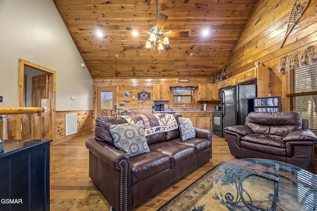 living area featuring visible vents, light wood-style flooring, a ceiling fan, and wood walls