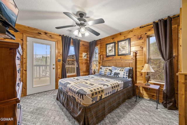 bedroom featuring wooden walls, access to exterior, a textured ceiling, and carpet floors