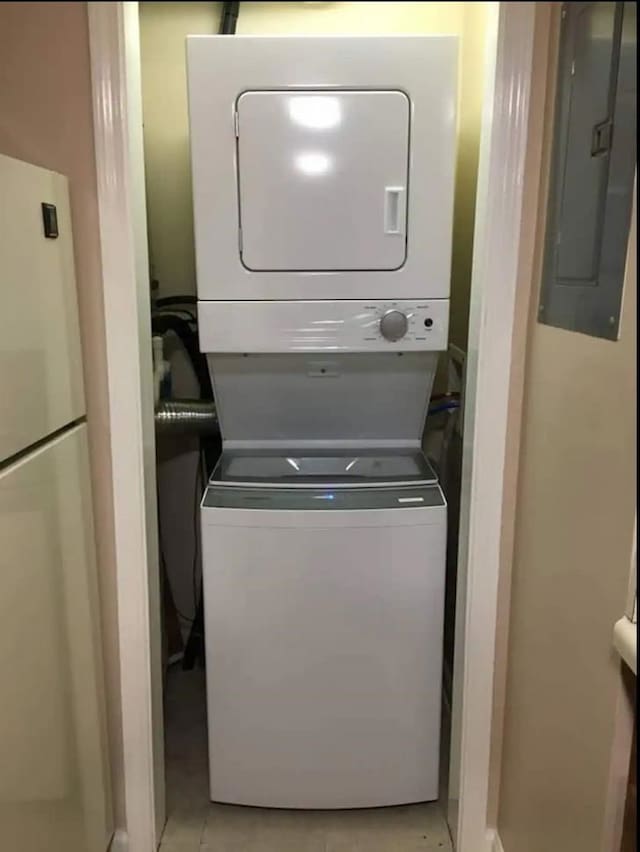 clothes washing area featuring electric panel, stacked washer / drying machine, and light tile patterned flooring