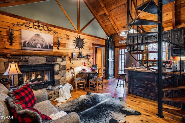 living room with wooden ceiling, a stone fireplace, hardwood / wood-style flooring, beamed ceiling, and wood walls