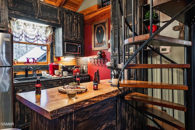 kitchen with dark cabinets, butcher block counters, black appliances, lofted ceiling, and a sink