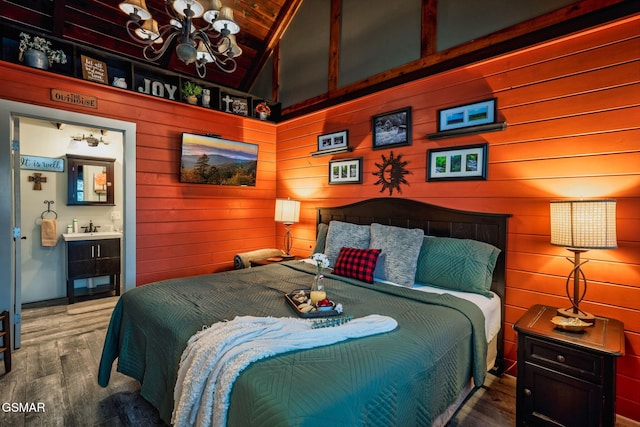 bedroom featuring a notable chandelier, a sink, wooden walls, connected bathroom, and wood finished floors