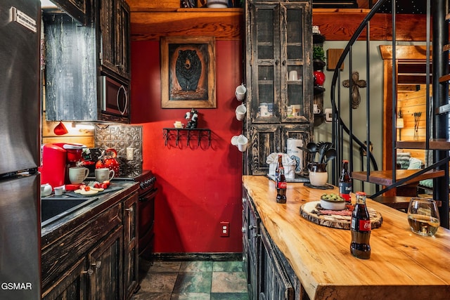kitchen featuring freestanding refrigerator, butcher block counters, black / electric stove, stainless steel microwave, and stone finish flooring