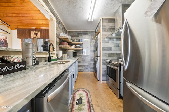 kitchen with a sink, a textured ceiling, light wood-type flooring, stacked washer and clothes dryer, and appliances with stainless steel finishes