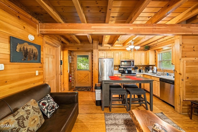 kitchen featuring light brown cabinets, wood walls, sink, beamed ceiling, and stainless steel appliances